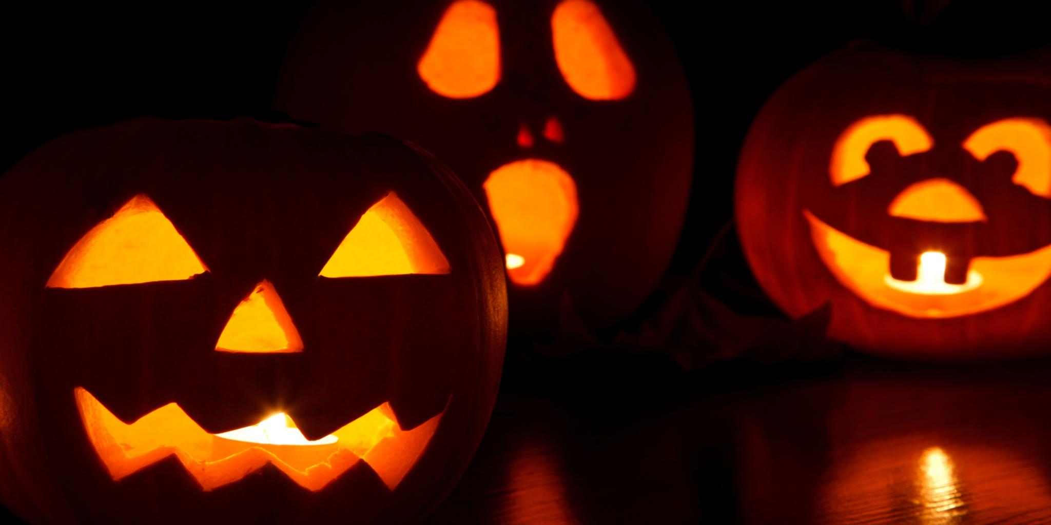 Drei leuchtende Halloween-Kürbisse mit geschnitzten Gesichtern auf dunklem Hintergrund.
