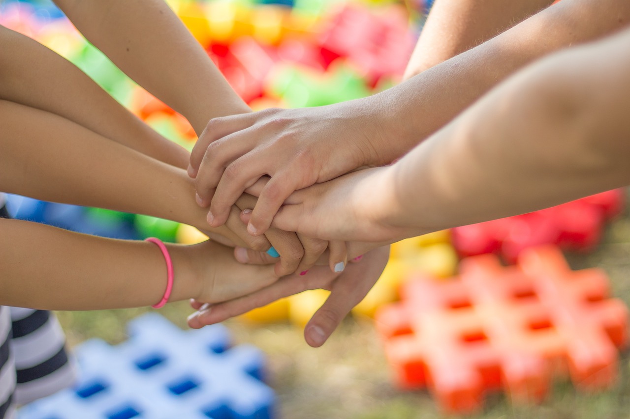 mehrere Kinder legen die Hände übereinander als Zeichen von Gemeinschaft
