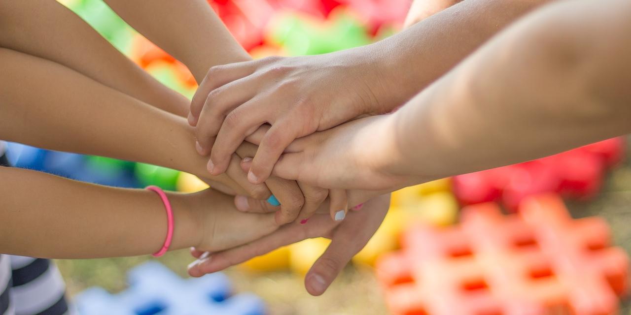 mehrere Kinder legen die Hände übereinander als Zeichen von Gemeinschaft