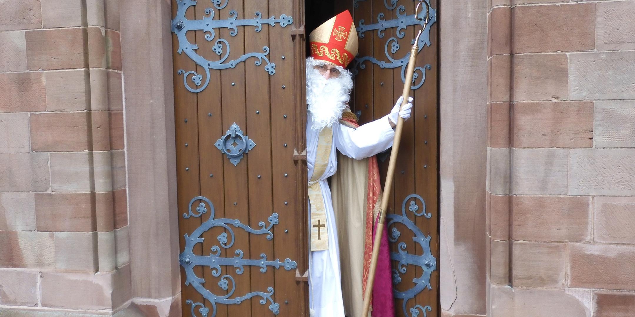 Nikolaus Nikolaus schaut aus einem halb geöffneten Kirchenportal aus der Kirche heraus