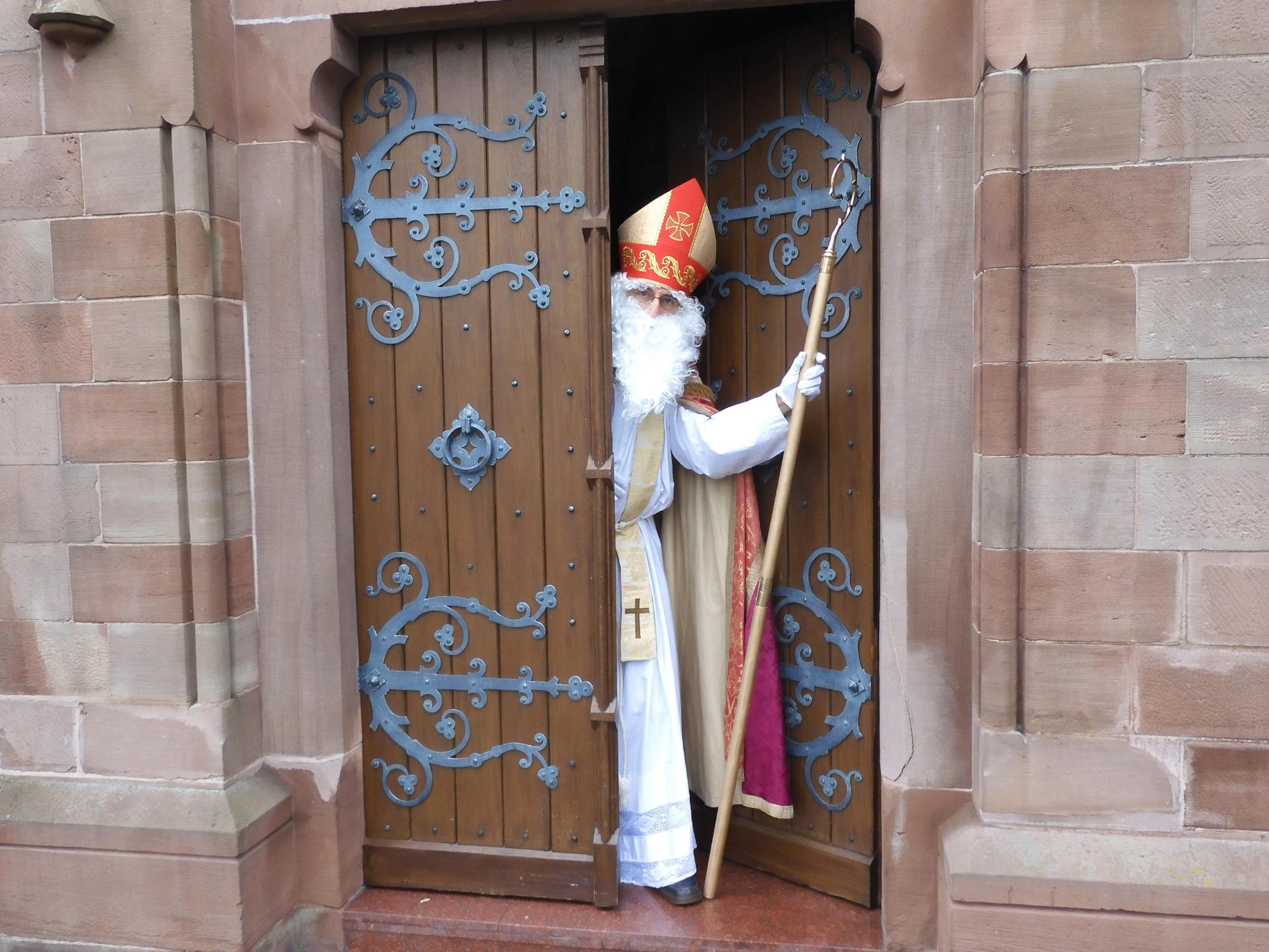 Nikolaus schaut aus einem halb geöffneten Kirchenportal aus der Kirche heraus